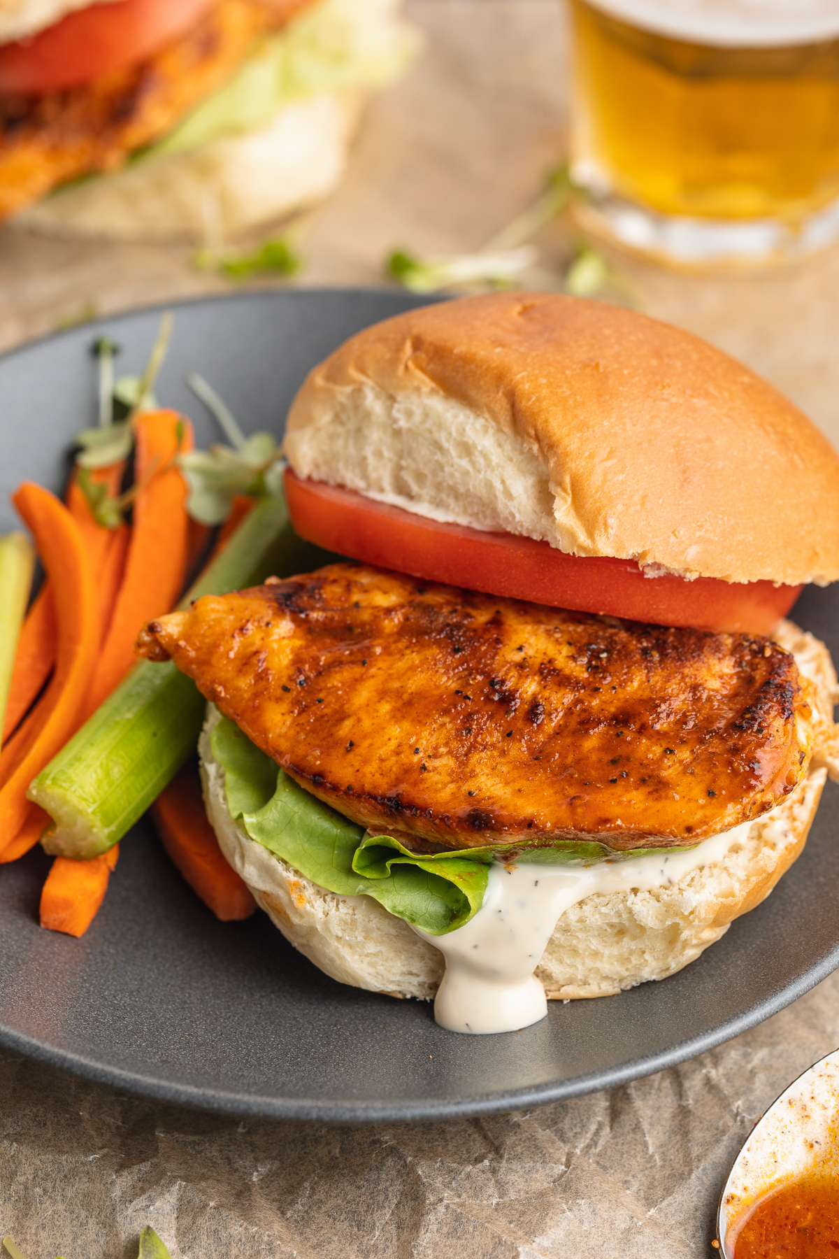 Overhead, angled view of a buffalo chicken sandwich on a plate. The top bun and slice of tomato are slightly askew.