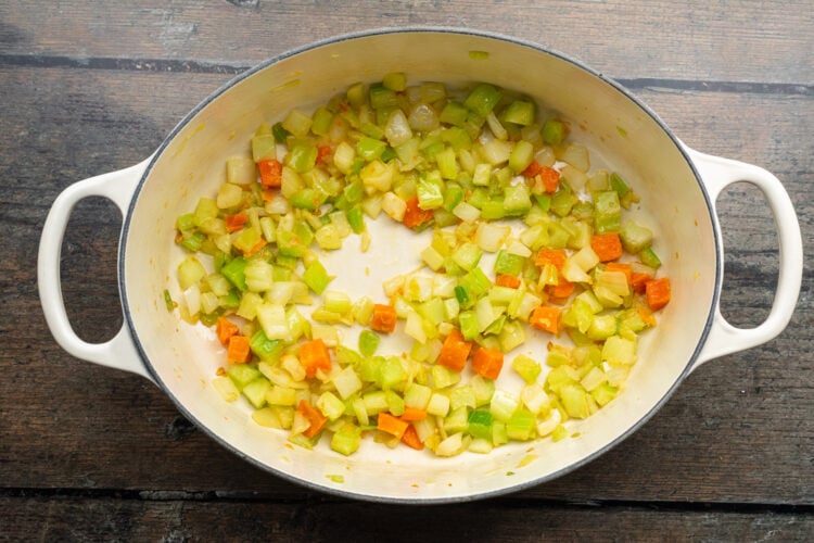 Overhead view of a large soup pot with butter, onion, celery, carrots, and garlic on a wooden table.