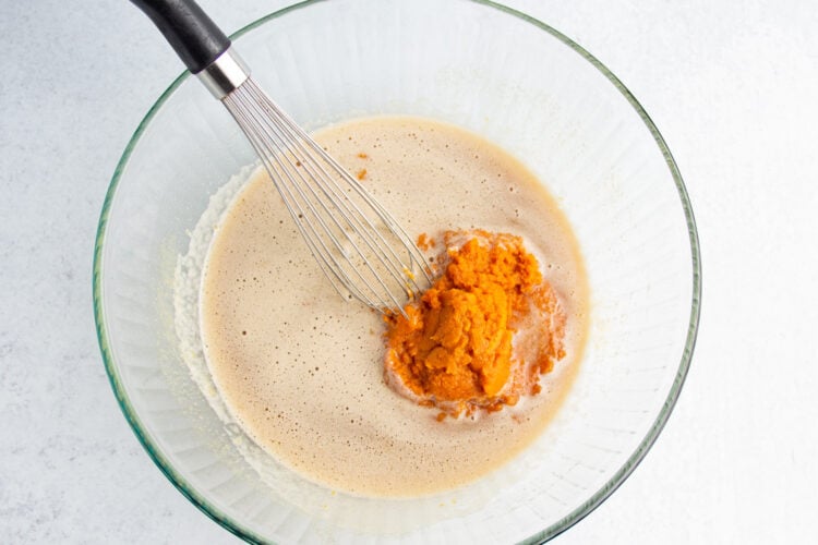 Overhead view of wet ingredients for gluten-free pumpkin bread plus pumpkin puree in a large glass mixing bowl with a whisk.