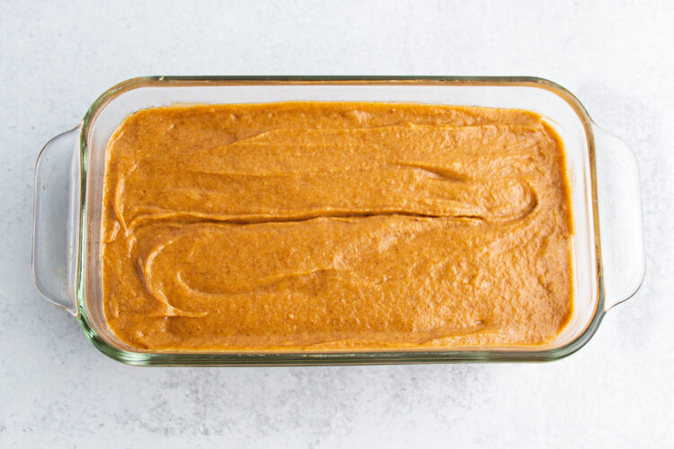 Overhead view of gluten-free pumpkin bread dough in a rectangular glass baking dish on a white tabletop.