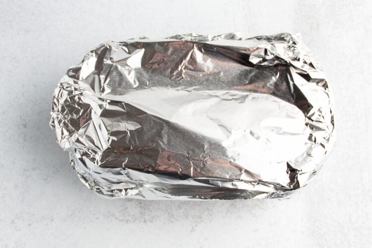 Overhead view of a rectangular baking dish containing gluten-free pumpkin bread dough covered with a sheet of aluminum foil.