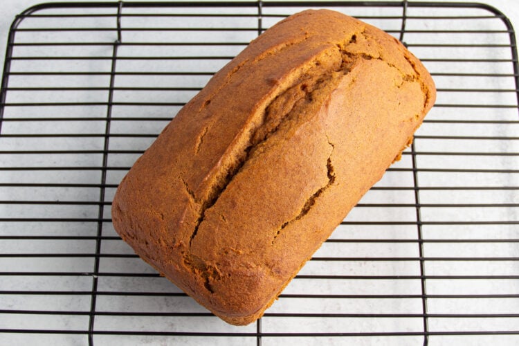 Overhead view of gluten-free pumpkin bread on a wire cooling rack. Bread is slightly split down center and deep orange in color.
