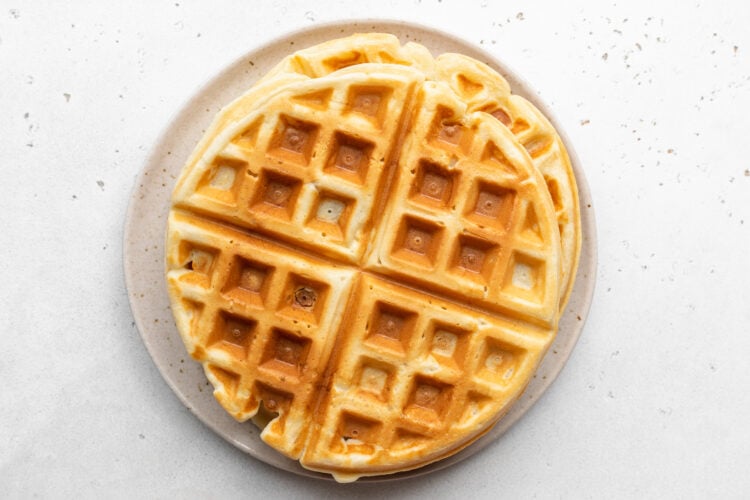 Overhead view of gluten-free waffles stacked on a plate. The waffles are large and round, divided into 4 wedges still connected.