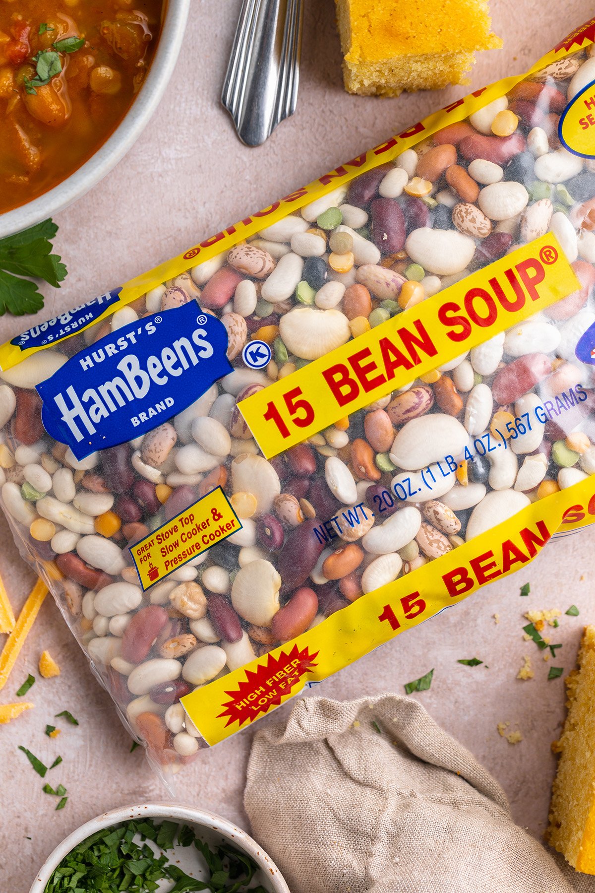 Hurst HamBeens 15-bean soup mix in branded packaging on a table with cornbread and 15-bean soup.