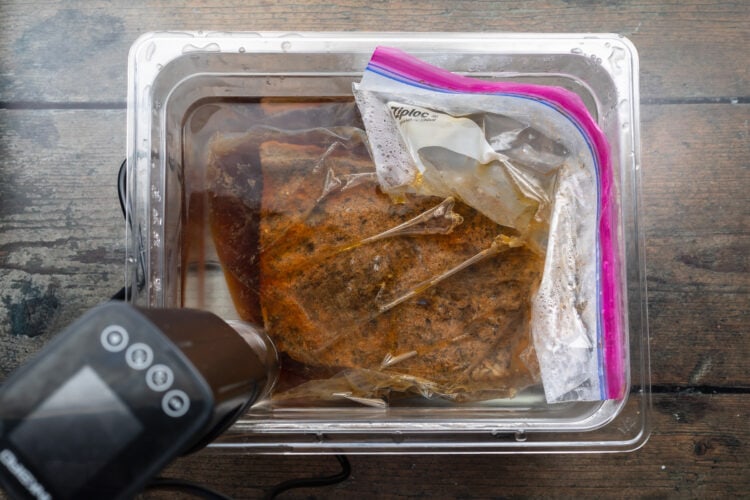 Seasoned brisket in a plastic bag, submerged in a water bath with a sous vide circulator.