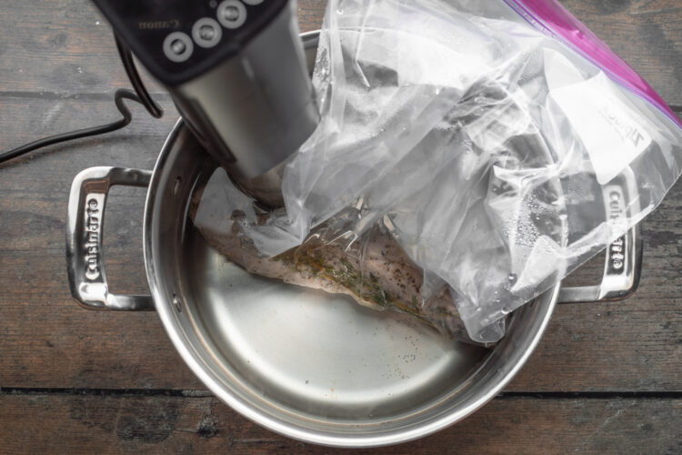 Overhead view of pork tenderloin in a gallon ziploc bag, lowered into a large pot with water and a sous vide circulator.