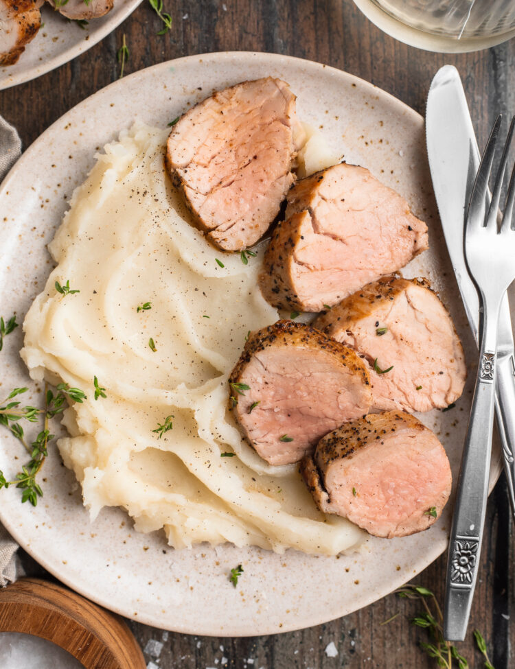 Overhead view of sous vide pork tenderloin sliced and plated with fluffy mashed potatoes on a wooden table.