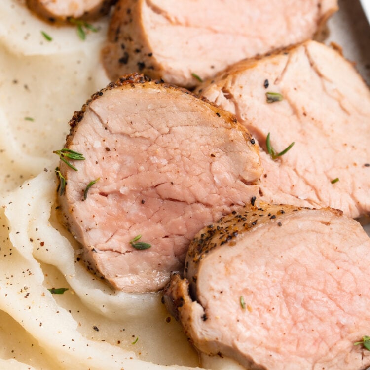 Sliced sous vide pork tenderloin on a white plate with a bed of fluffy whipped mashed potatoes.