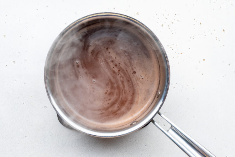 Overhead view of au jus mixture in a silver saucepan on a white countertop.