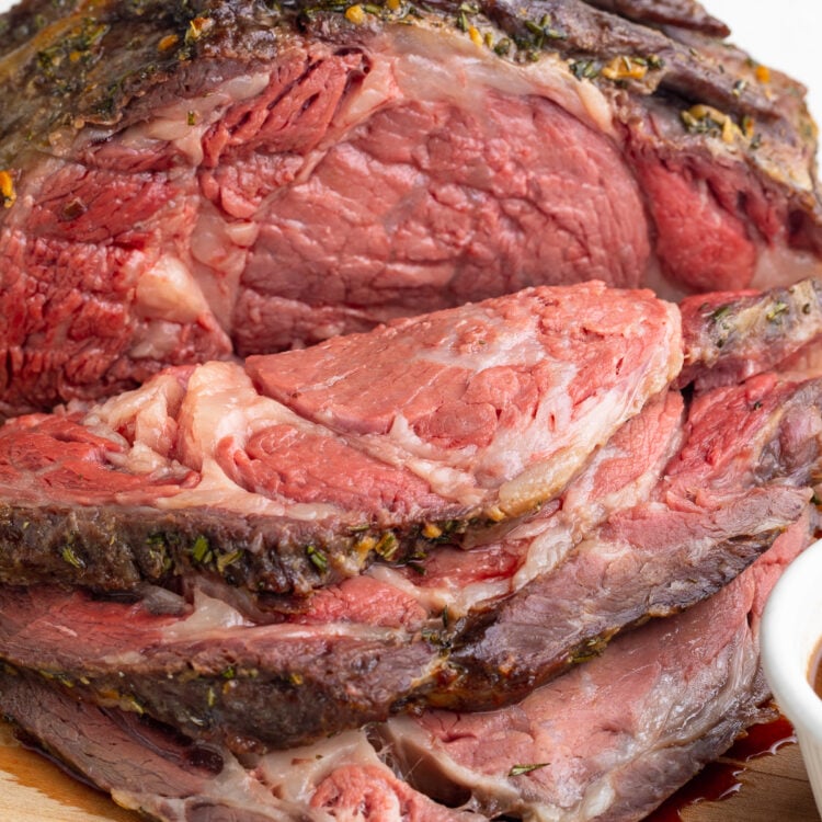 Close-up look at a carved sous vide prime rib on a wooden cutting board in front of a white background.