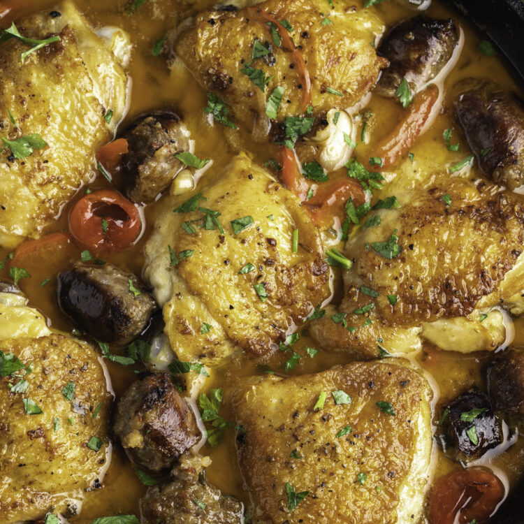 Zoomed out overhead view of chicken scarpariello in a large black cast-iron skillet.