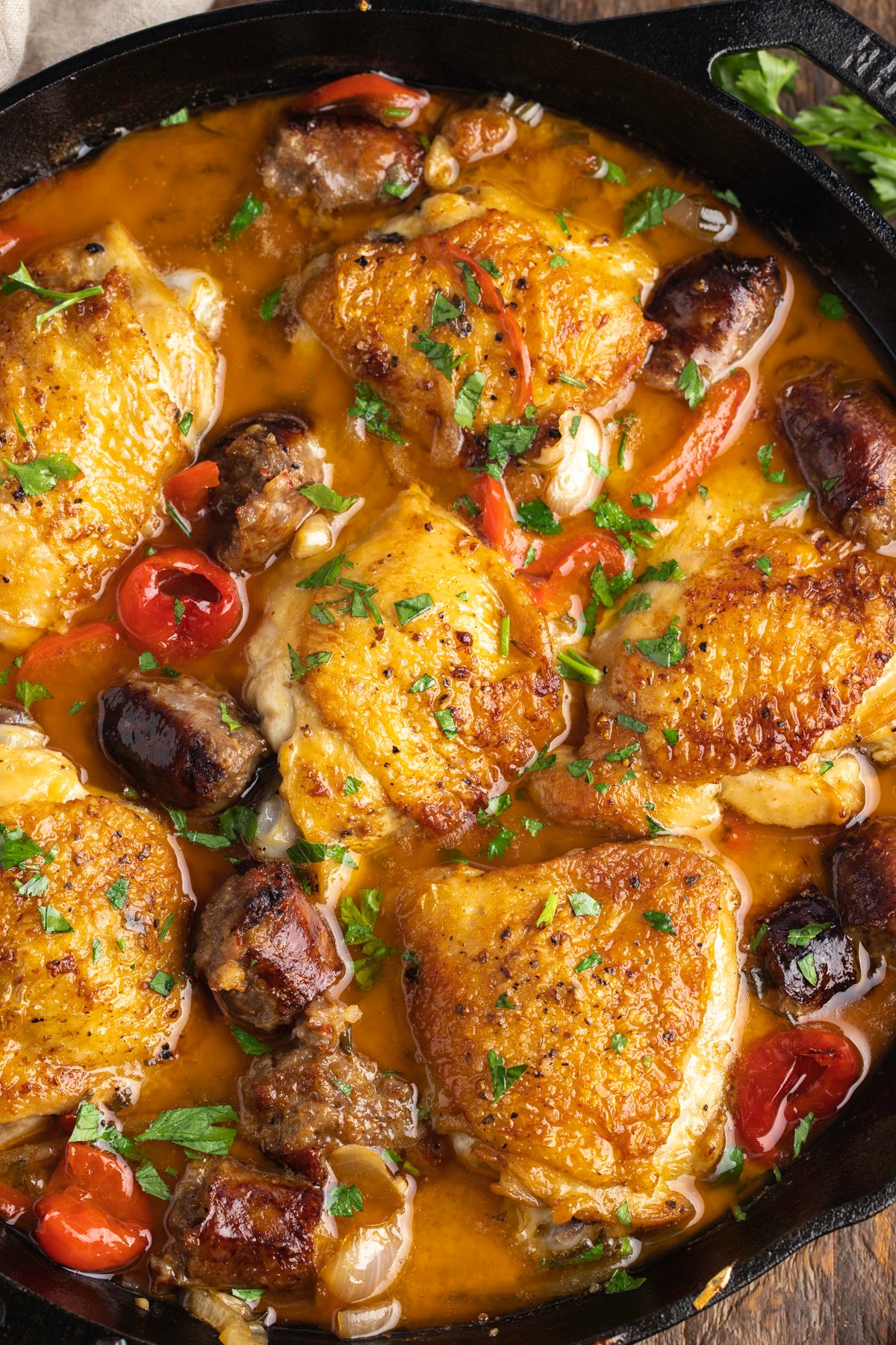 Zoomed out overhead view of chicken scarpariello in a large black cast-iron skillet.