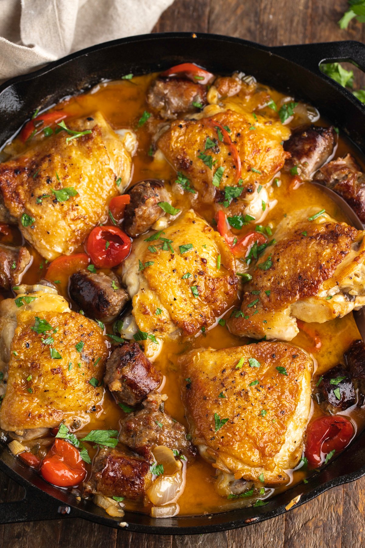 Zoomed out overhead view of chicken scarpariello in a large black cast-iron skillet.
