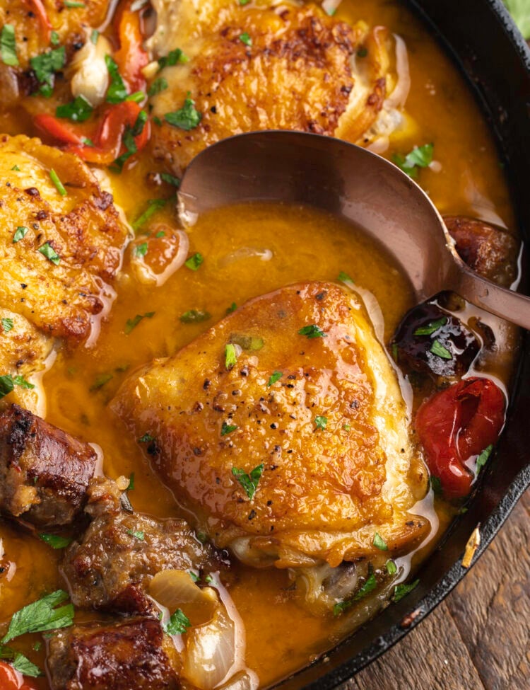 Overhead view of chicken scarpariello in a large cast iron skillet with a spoon on a wooden background.