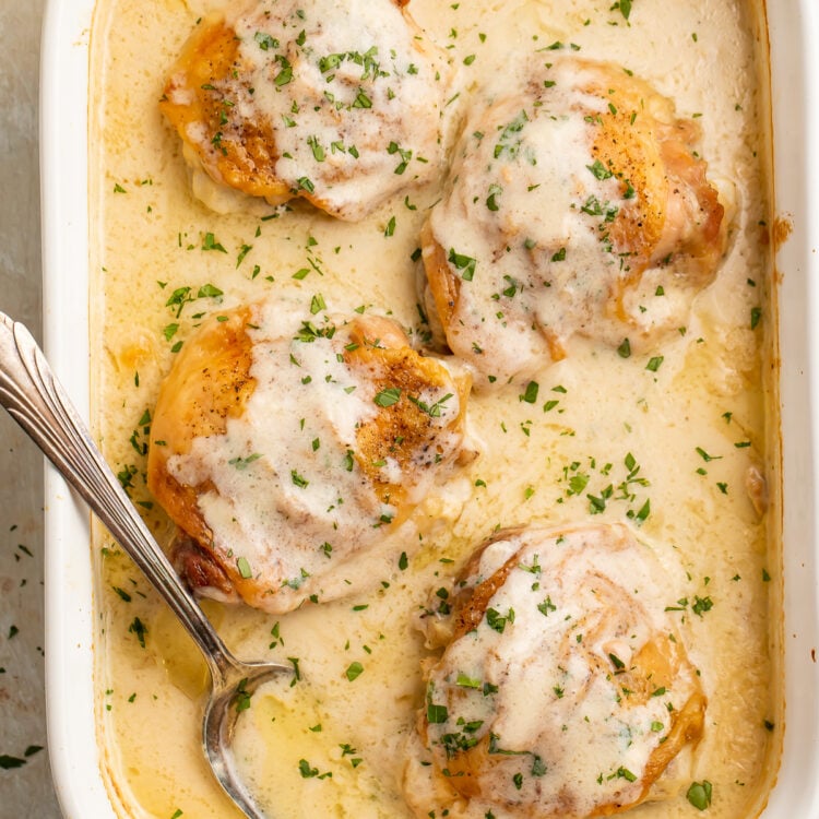 Overhead view of 4 chicken thighs in a large rectangular casserole dish with a spoon resting in a sauce of cream of chicken soup and milk.