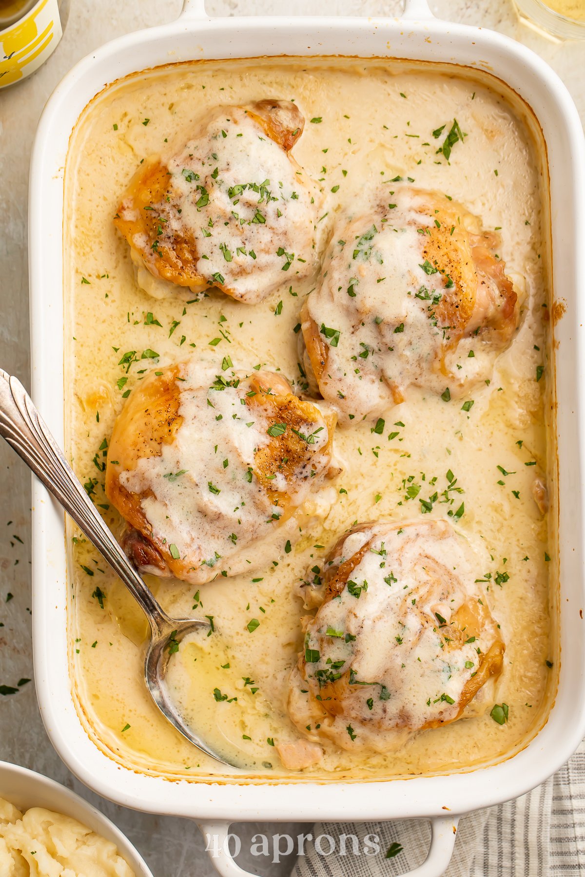 Overhead view of 4 chicken thighs in a large rectangular casserole dish with a spoon resting in a sauce of cream of chicken soup and milk.