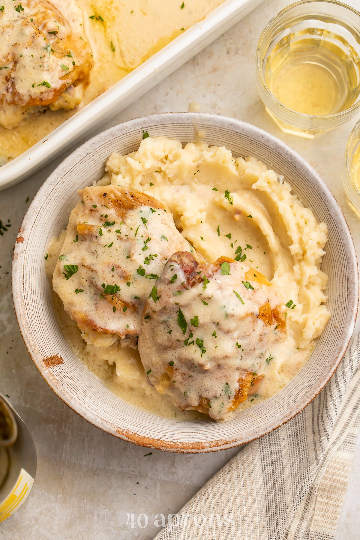 Overhead view of a bowl of chicken soup chicken over a bed of creamy mashed potatoes, with a casserole dish of chicken in the background.