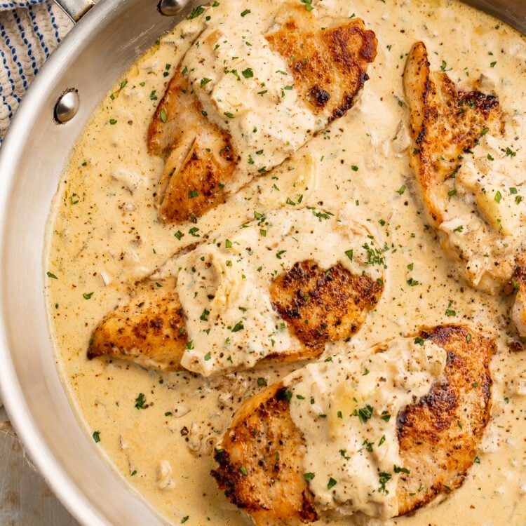 Overhead view of 4 chicken breasts in a creamy garlic sauce in a large silver skillet.