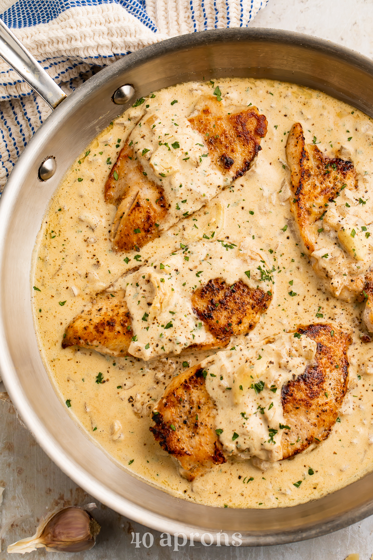Overhead view of 4 chicken breasts in a creamy garlic sauce in a large silver skillet.