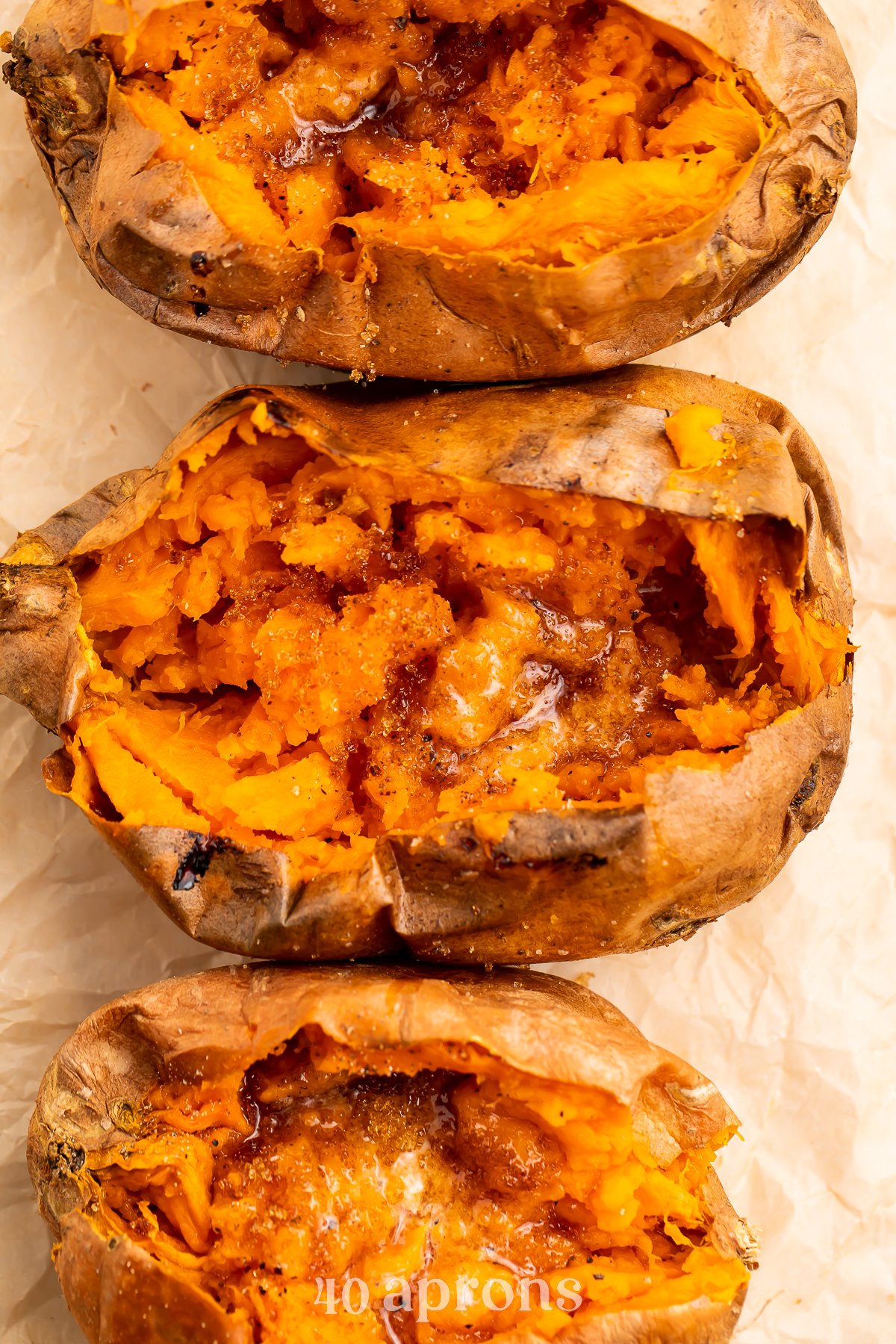 Overhead view of a vertical row of cut-open sweet potatoes on a sheet of parchment paper.