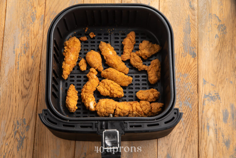 Overhead view of frozen chicken tenders in an air fryer basket.