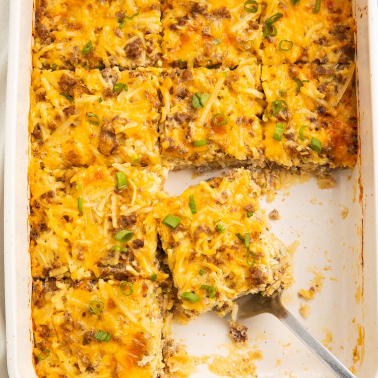 Overhead view of a rectangular casserole dish with 9 squares of gluten free breakfast casserole. A silver server rests under one square of casserole.