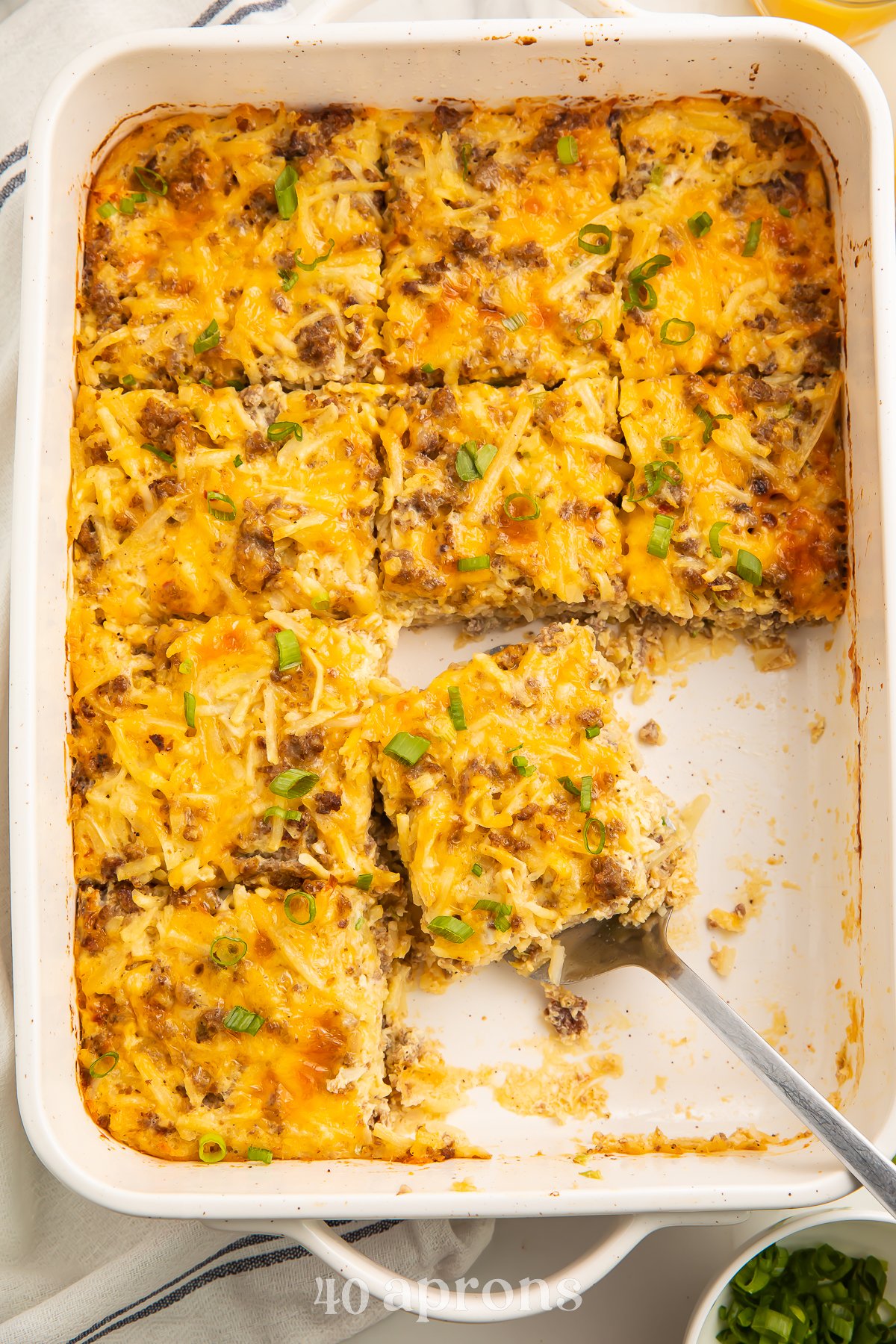 Overhead view of a rectangular casserole dish with 9 squares of gluten free breakfast casserole. A silver server rests under one square of casserole.