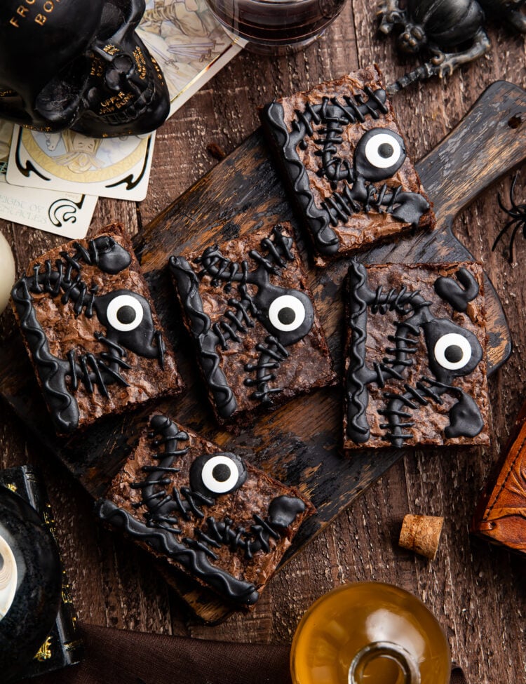 Overhead view of 5 Hocus Pocus spellbook brownies on a wooden tray surrounded by Halloween imagery.