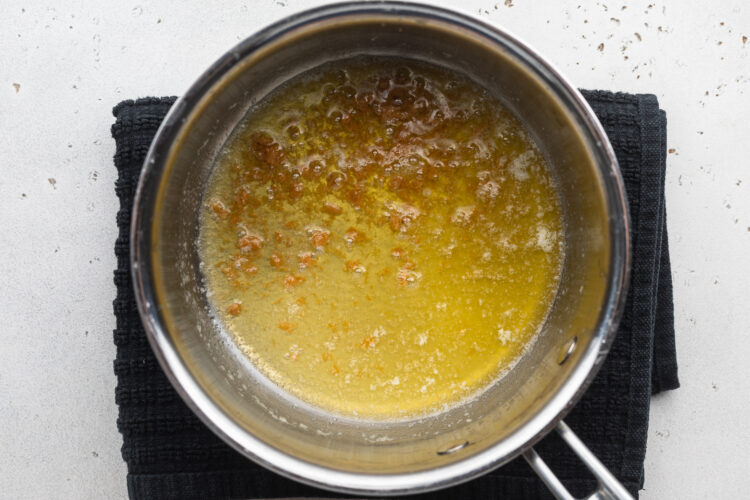 Overhead view of a small silver saucepan with melted butter on an electric burner.