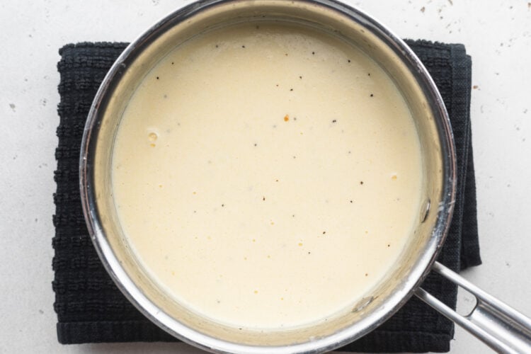 Overhead view of creamy, thick alfredo sauce with heavy cream, parmesan, and asiago cheese in a silver saucepan.