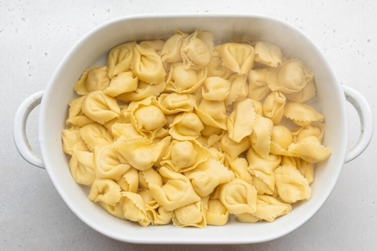 Overhead view of cooked tortelloni in a large oval baking dish on a neutral countertop.