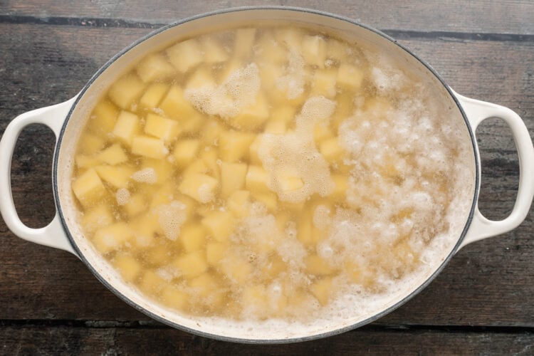 Overhead view of cubed potatoes in salted boiling water in a handled baking dish.
