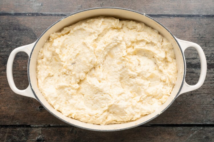 Overhead view of creamy, cheesy mashed potatoes in a large oval baking dish with handles on each end.
