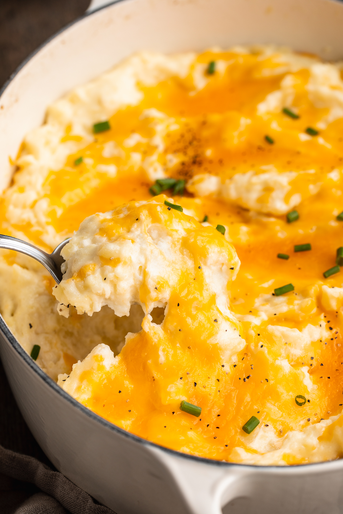 Side view of a scoop of cheesy mashed potatoes being lifted out of a large casserole dish with a spoon.