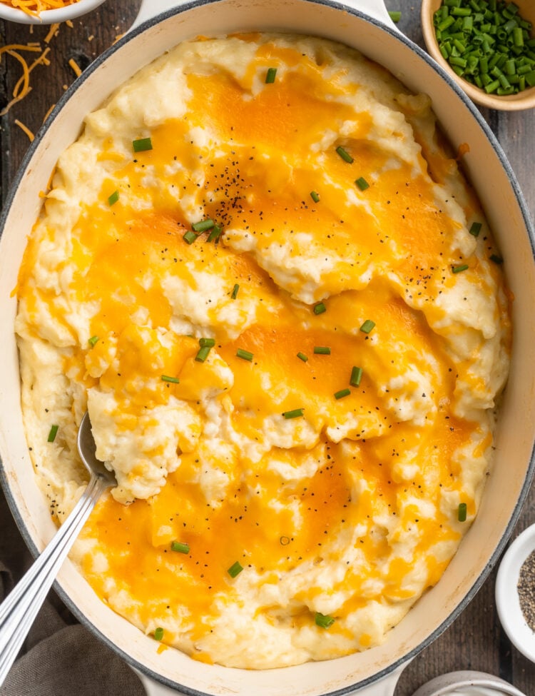 Overhead view of a large oval dish holding fluffy, creamy, cheesy mashed potatoes topped with cheddar cheese.