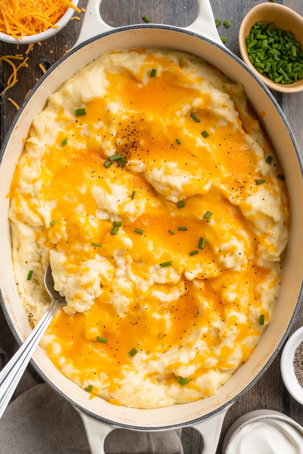 Overhead view of a large oval dish holding fluffy, creamy, cheesy mashed potatoes topped with cheddar cheese.