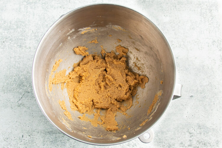 Overhead view of creamed butter and sugars in a large silver mixing bowl.