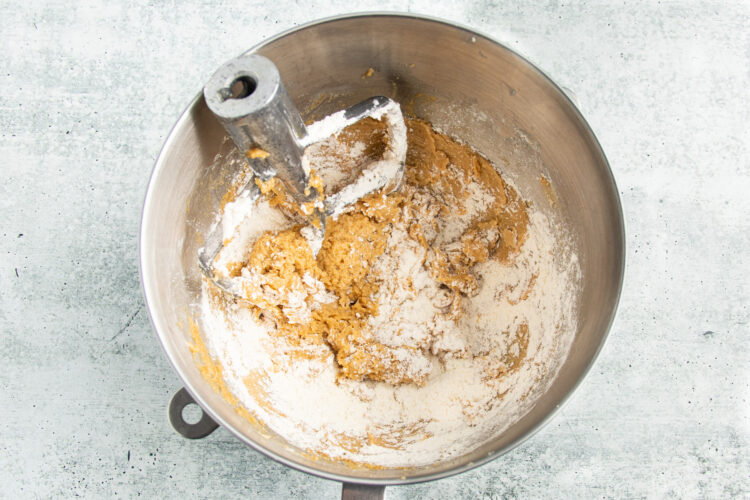Overhead view of flour mixture added to creamed butter and sugars in a large silver mixing bowl.