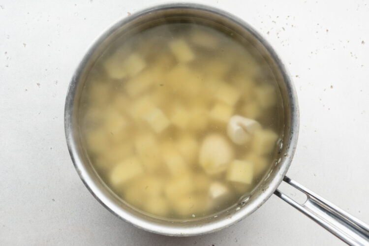 Overhead view of cubed potatoes covered with salted water in a silver saucepan with single handle.