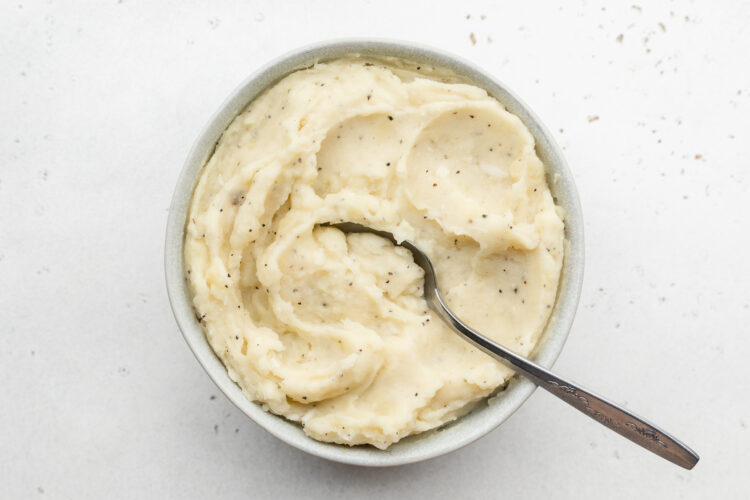 Overhead view of creamy dairy-free mashed potatoes in a large white bowl with a silver spoon.
