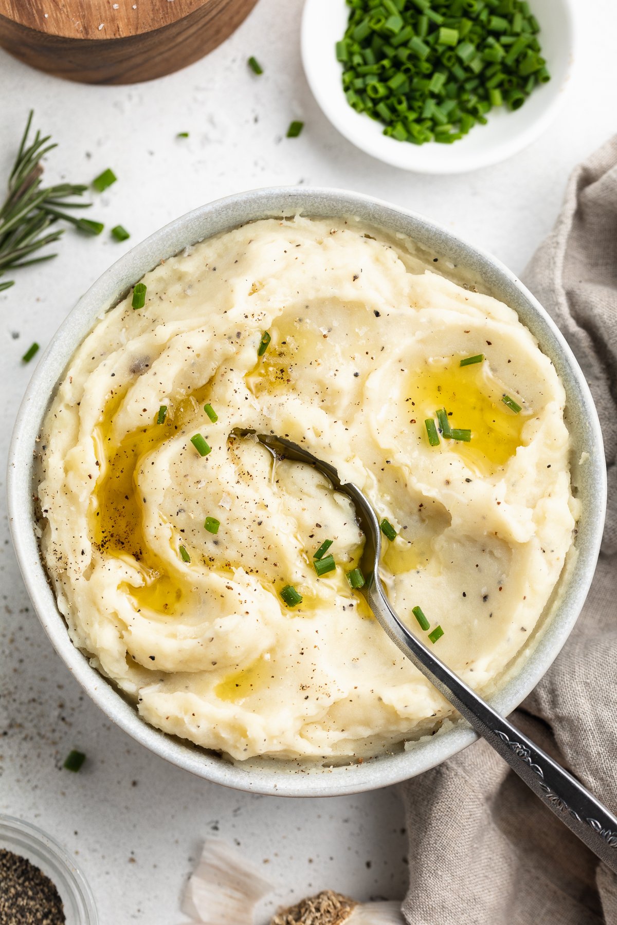 Overhead view of a bowl of dairy-free mashed potatoes on a white table top. A silver spoon rests in the potatoes.