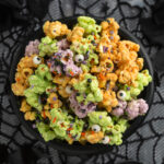 Overhead view of a plastic cauldron filled with orange, purple, and green white chocolate covered popcorn clusters with sprinkles and candy eyes.