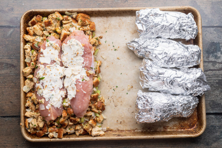 Overhead view of foil-wrapped sweet potatoes and butter-topped turkey loin atop a bread stuffing on a baking sheet.