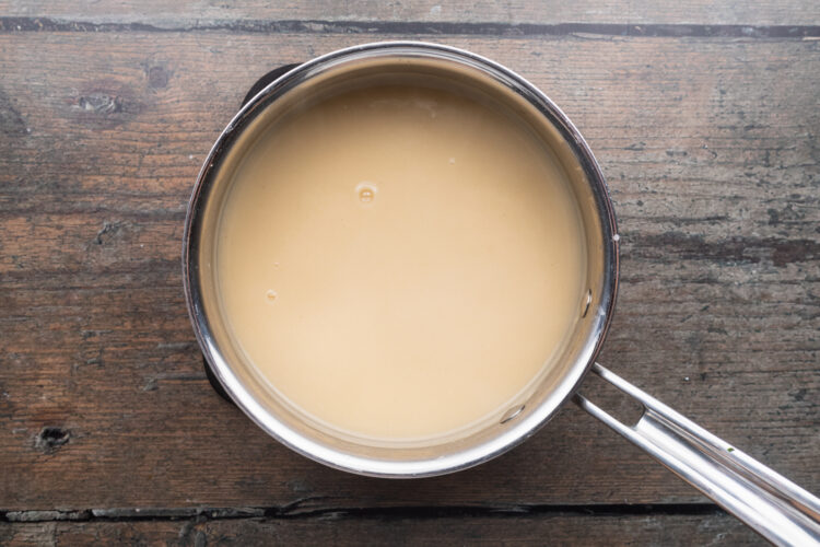 Overhead view of a small silver saucepan containing a thick, white flour-based gravy for a Thanksgiving meal.