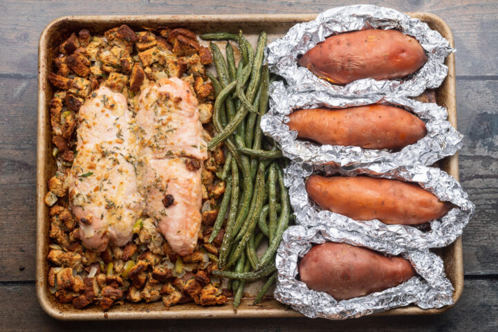 Overhead view of a fully-prepared one-pan holiday meal of turkey, stuffing, green beans, and sweet potatoes on a baking sheet.