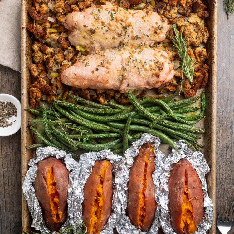 Overhead view of a sheet pan filled with green beans, turkey, foil-wrapped sweet potatoes, and stuffing.