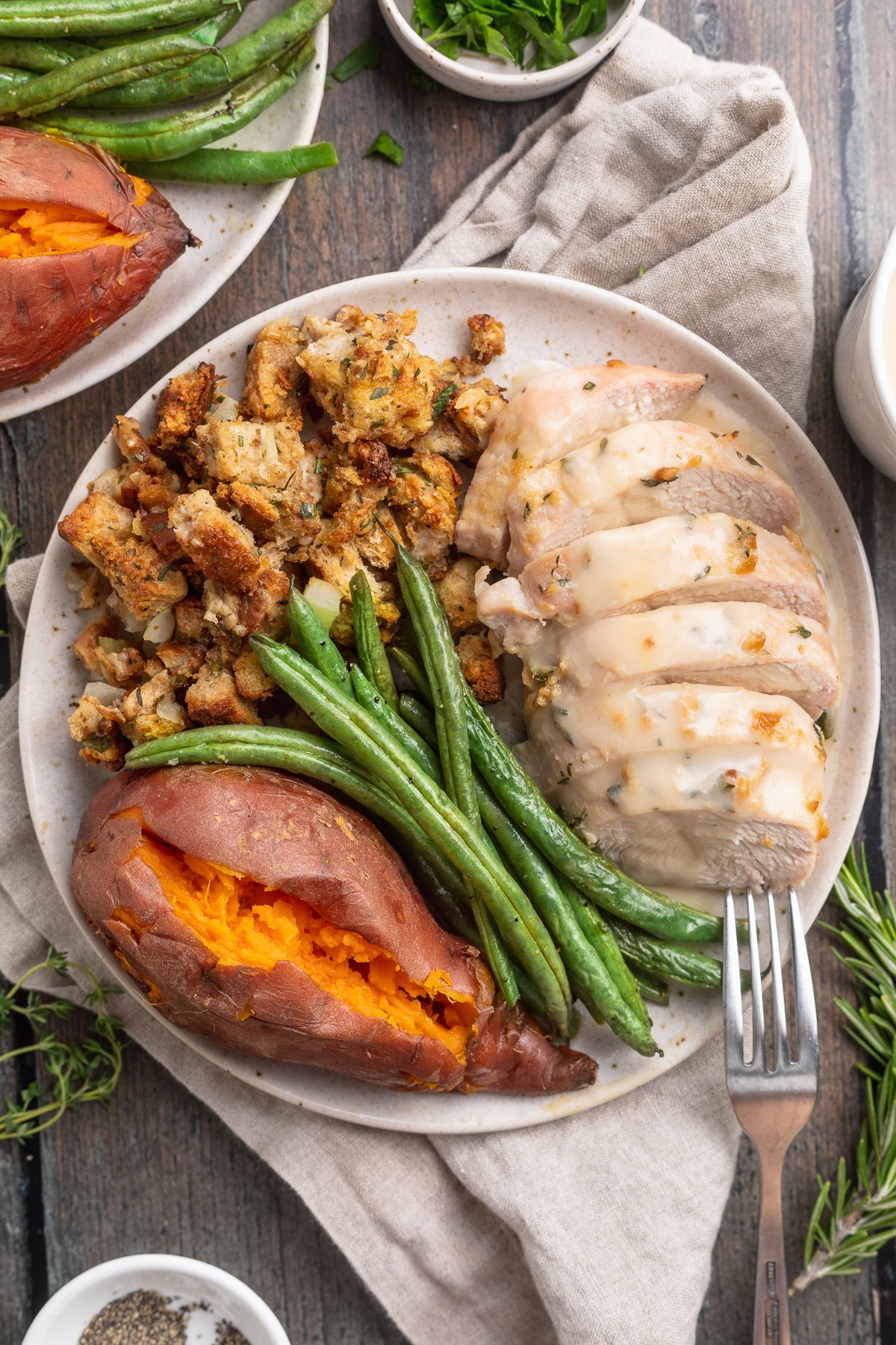 Overhead view of a one pan holiday meal fully plated on a round dinner plate, showcasing turkey, stuffing, green beans, and sweet potatoes.