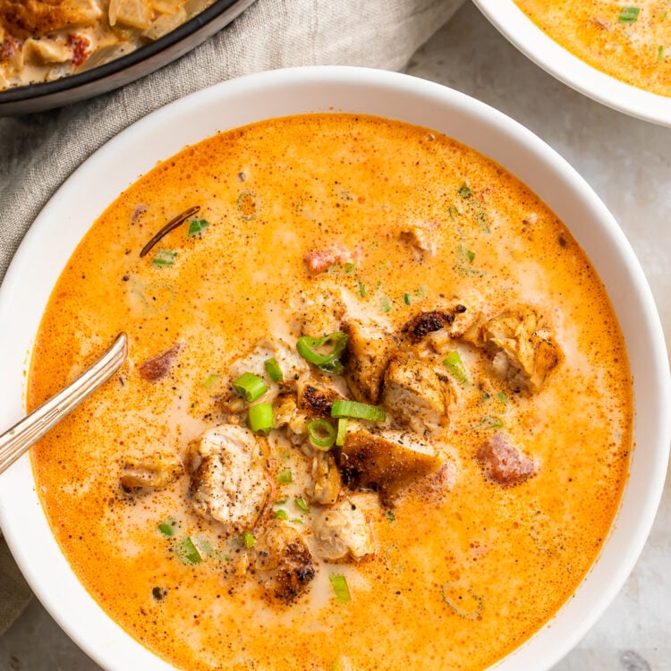 Overhead, zoomed-in view of a bowl of creamy cajun chicken soup in a white soup bowl with a silver spoon on a marble countertop.