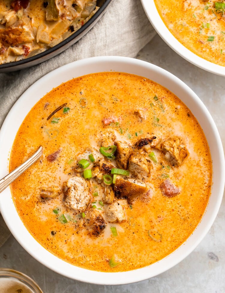 Overhead, zoomed-in view of a bowl of creamy cajun chicken soup in a white soup bowl with a silver spoon on a marble countertop.