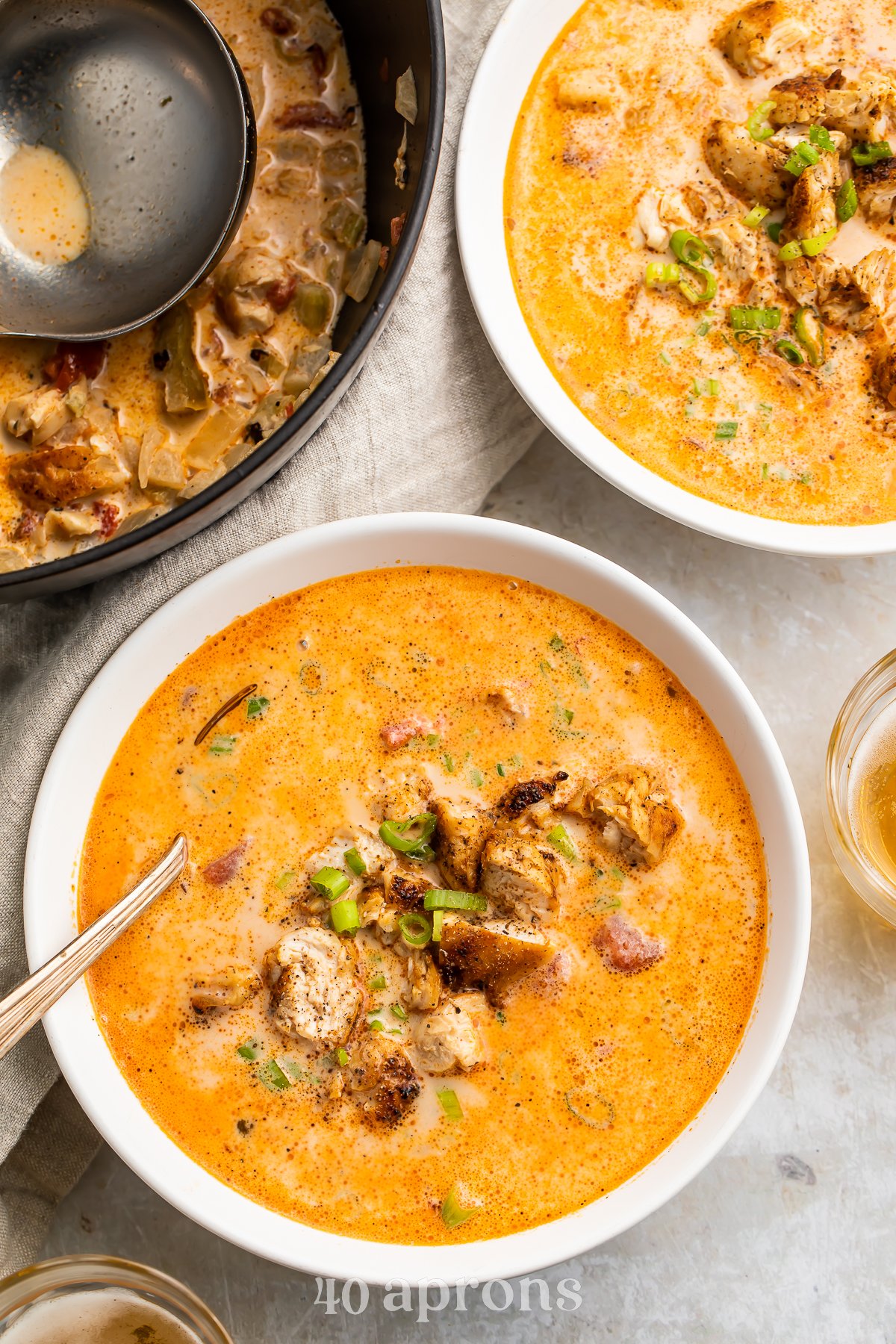 Overhead, zoomed-out view of a bowl of creamy cajun chicken soup in a white soup bowl with a silver spoon on a marble countertop.